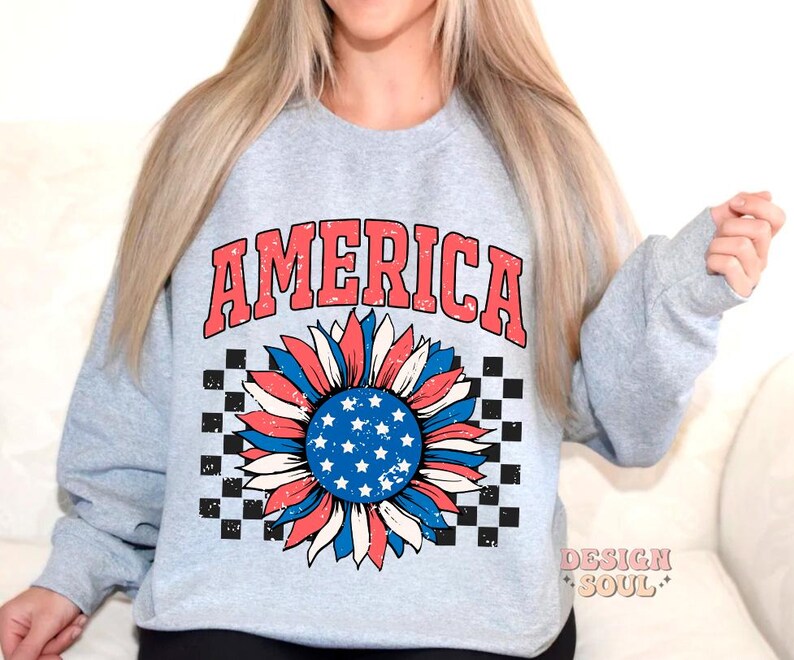 May include: A light gray sweatshirt with the word "AMERICA" printed in red and blue letters. A red, white, and blue sunflower with a checkered background is printed below the word.