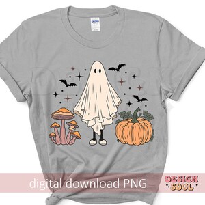 May include: A gray t-shirt with a white ghost, mushrooms, and a pumpkin. The ghost is wearing a white sheet and has a friendly face. The mushrooms are brown and white with orange tops. The pumpkin is orange with a green stem. The text "digital download PNG" is at the bottom of the shirt.