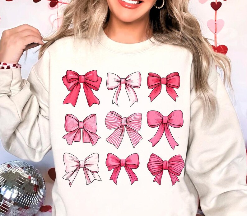 May include: A white sweatshirt with a pink and white bow pattern. The bows are arranged in a grid of nine.