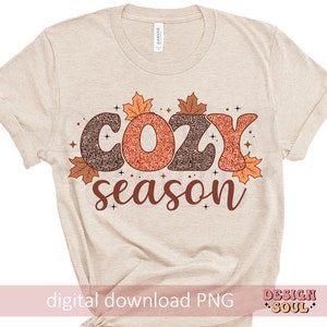 May include: Beige t-shirt with the words "COZY season" in brown and orange glitter lettering, decorated with fall leaves. The words "digital download PNG" are at the bottom. The shirt is a casual style.