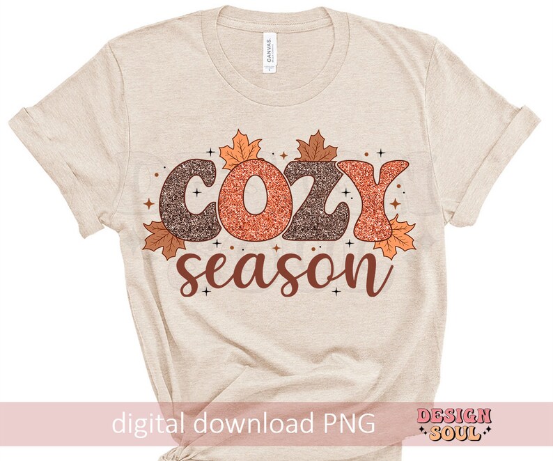 May include: Beige t-shirt with the words "COZY season" in brown and orange glitter lettering, decorated with fall leaves. The words "digital download PNG" are at the bottom. The shirt is a casual style.
