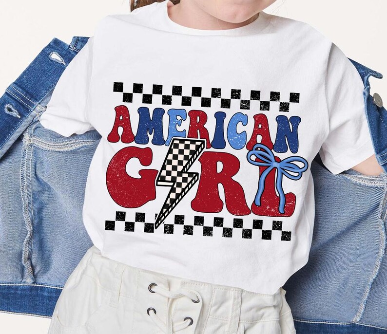 May include: White t-shirt with a red, white, and blue graphic that says "American Girl" with a lightning bolt and a blue bow. The graphic is surrounded by a black and white checkered pattern.