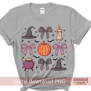 Puede incluir: Una camiseta gris con un dise&ntilde;o de varios elementos de tem&aacute;tica de Halloween, incluyendo un sombrero de bruja, una calabaza, una vela y lazos. El dise&ntilde;o est&aacute; en tonos de rosa, gris y naranja.