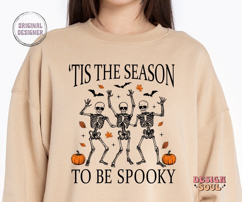May include: Tan sweatshirt with a graphic of three skeletons dancing with the text 'Tis the season to be spooky' and two pumpkins on either side.