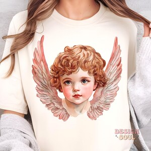 Op de afbeelding: Een wit T-shirt met een vintage illustratie van een cherubijn met roze vleugels. De cherubijn heeft krullend rood haar en blauwe ogen.