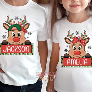 May include: Two white t-shirts with a Christmas reindeer design. The reindeer is wearing a red hat and a red bow. The text "Jackson" and "Amelia" are on the shirts.
