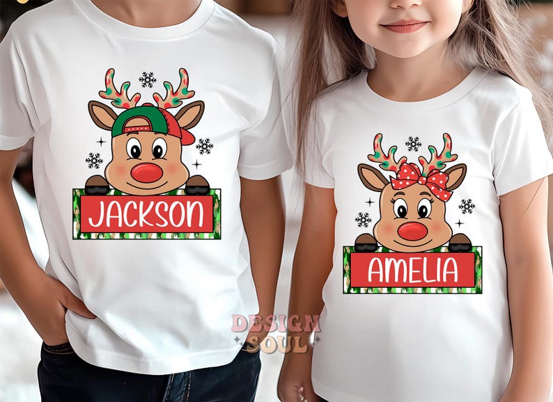 May include: Two white t-shirts with a Christmas reindeer design. The reindeer is wearing a red hat and a red bow. The text "Jackson" and "Amelia" are on the shirts.