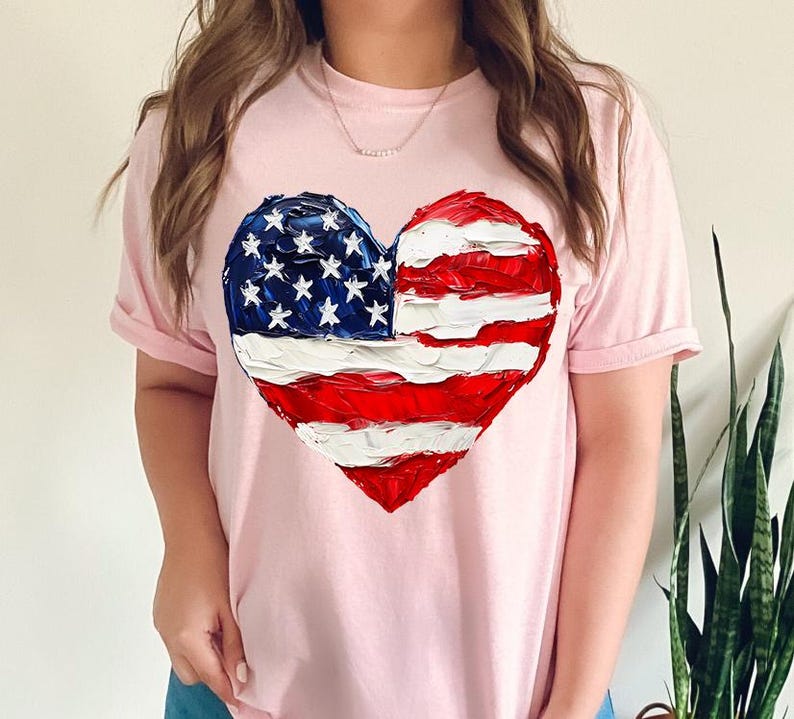 Pu&ograve; includere: Una maglietta rosa con una bandiera americana dipinta a forma di cuore.