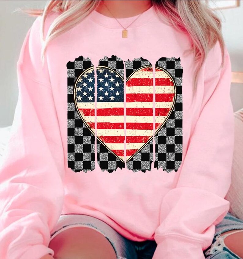 May include: Pink sweatshirt with a distressed American flag heart design on a black and white checkered background.