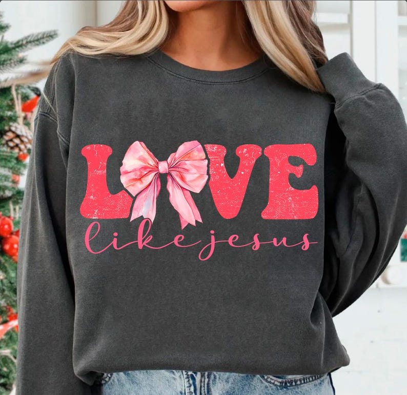 May include: A dark grey sweatshirt with the word "LOVE" in red featuring a pink bow in the centre and the words "like jesus" in white below.