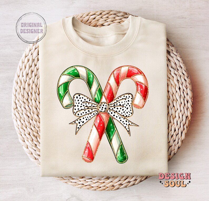 May include: A cream-colored sweatshirt with a design of two candy canes tied together with a black and white polka dot bow. The candy canes are red and white and green and white.