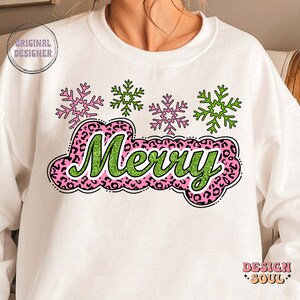 May include: White sweatshirt featuring a green and pink "Merry" graphic with a leopard print design. The graphic is surrounded by four snowflakes, two green and two pink.