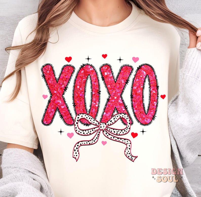 May include: A white t-shirt with a pink glitter XOXO design and a black and white polka dot bow. The shirt has a crew neck and short sleeves.