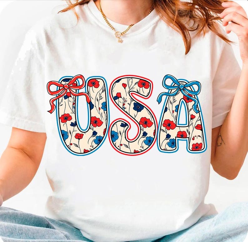May include: White t-shirt with a red, white, and blue floral design spelling out "USA".