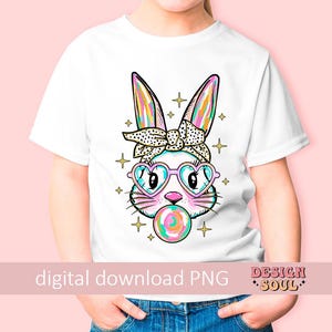 May include: A white t-shirt with a colorful graphic of a bunny wearing sunglasses and a headband. The bunny is holding a lollipop in its mouth. The graphic is surrounded by stars and sparkles.