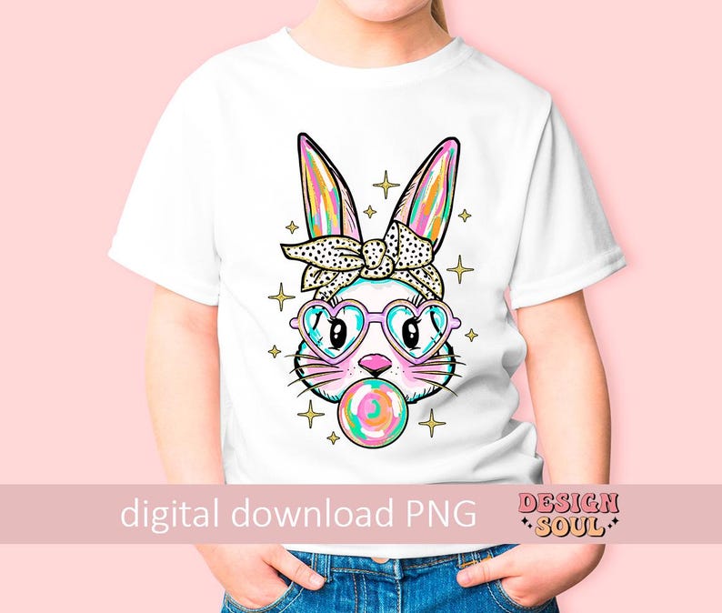 May include: A white t-shirt with a colorful graphic of a bunny wearing sunglasses and a headband. The bunny is holding a lollipop in its mouth. The graphic is surrounded by stars and sparkles.