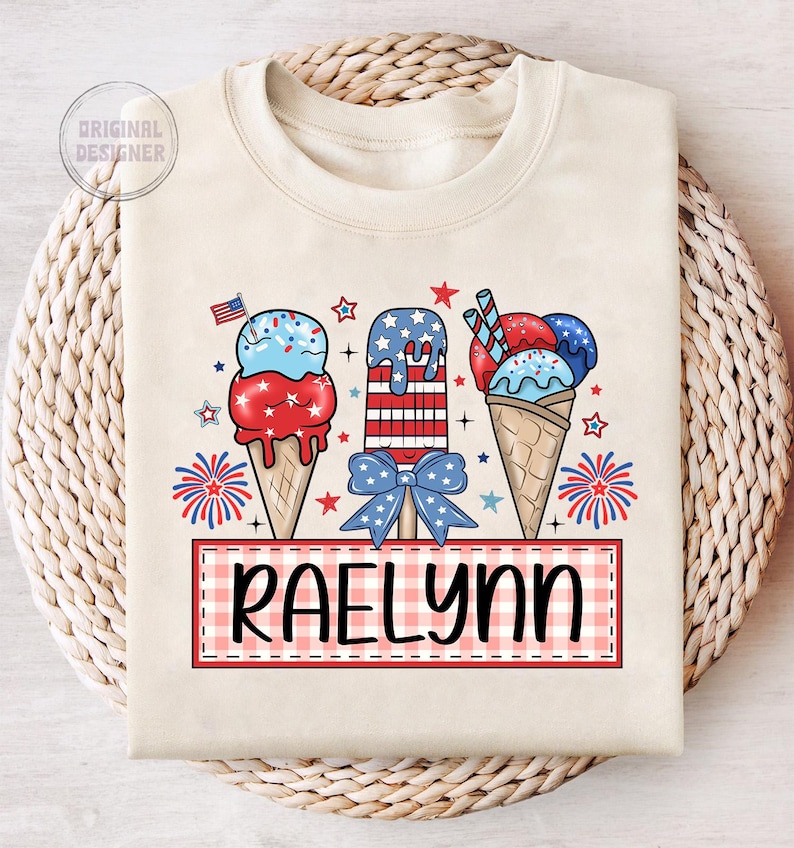 May include: A white t-shirt with a red, white, and blue ice cream cone design. The ice cream cones are decorated with stars and stripes. The text "RAELYN" is written in black on a red and white checkered background.