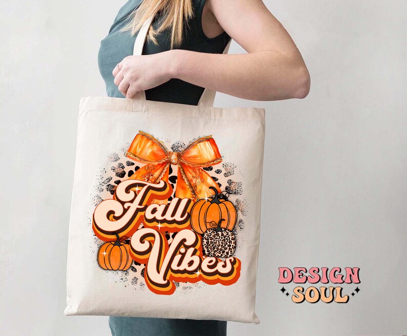 May include: A white tote bag with an orange and brown bow, pumpkins, and the text "Fall Vibes" in a retro font. The bag is made of canvas and has a brown leather handle.