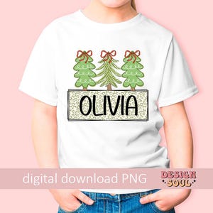 May include: White t-shirt with a design of three green Christmas trees with red bows and the name "Olivia" in a black and white leopard print box.