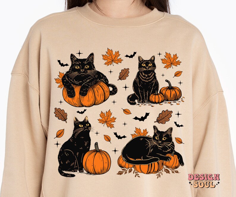 May include: Beige sweatshirt featuring a Halloween-themed design. The graphic includes four black cats, orange pumpkins, autumn leaves, and bats. The design has a vintage, cartoon-like style, perfect for fall.