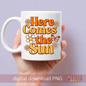 May include: White ceramic mug with a graphic design featuring orange and yellow flowers, a butterfly, and the text "Here Comes the Sun".