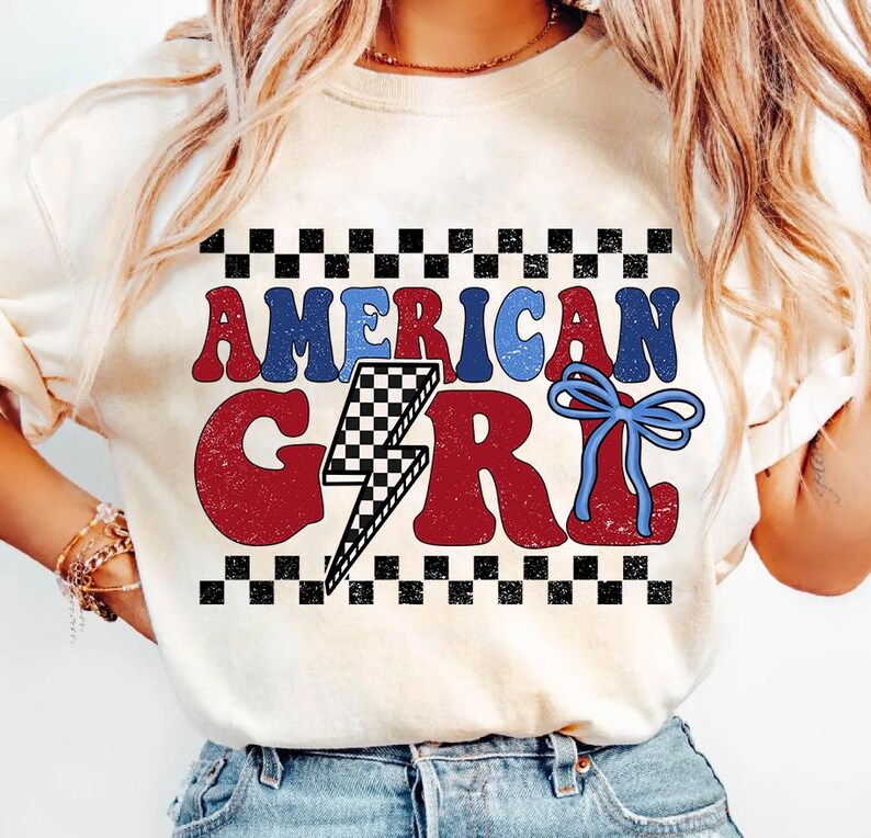 May include: A white t-shirt with a red, white, and blue graphic that says "American Girl" with a lightning bolt and a blue bow. The graphic is surrounded by a black and white checkered border.