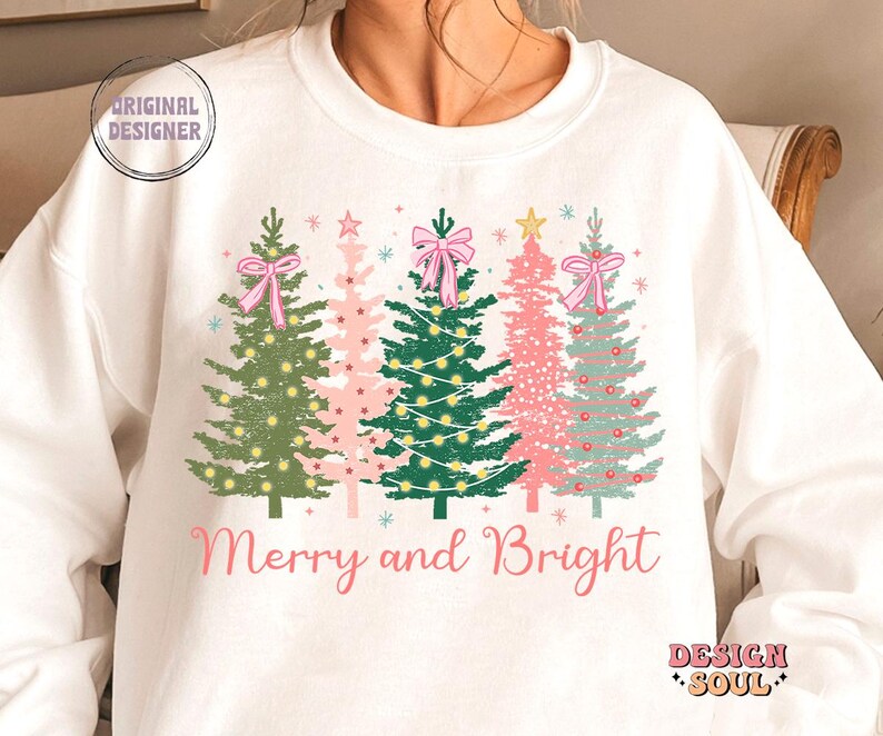 May include: White sweatshirt with a Christmas tree design and the text "Merry and Bright". The trees are green, pink, and blue with pink bows and white lights.
