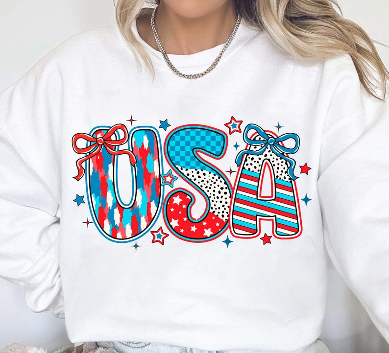 May include: White sweatshirt with a red, white, and blue USA graphic. The letters are decorated with stars, stripes, and polka dots.