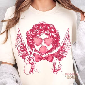 May include: A pink and white graphic design of a cherub with angel wings wearing heart-shaped sunglasses and blowing a bubble. The cherub is wearing a pink bow tie.