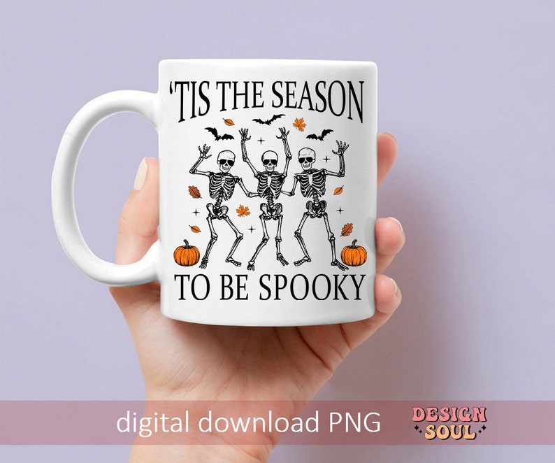 May include: White ceramic mug with a black graphic of three skeletons dancing with the text 'Tis the season to be spooky' and two orange pumpkins.