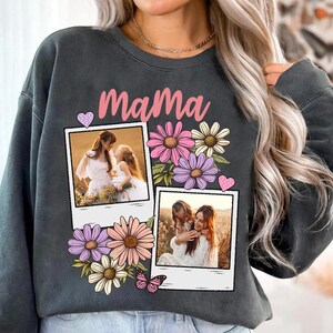 May include: Dark gray sweatshirt with the word "Mama" in pink script. The sweatshirt features two polaroid-style photos, floral accents, and a butterfly graphic. The photos show a mother and child.