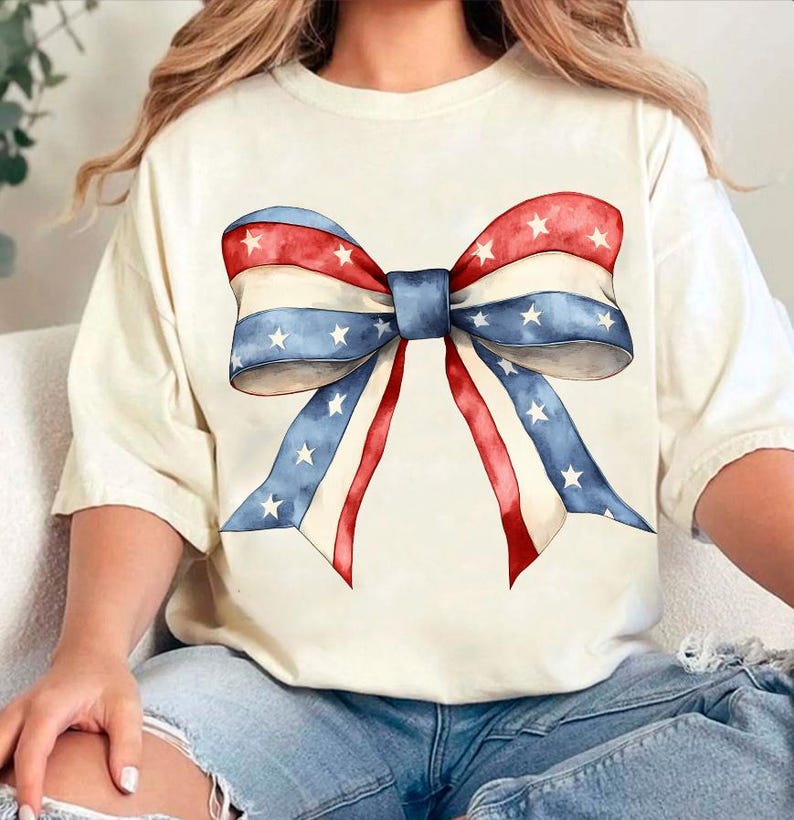 K&ouml;nnte beinhalten: Ein wei&szlig;es T-Shirt mit einer rot-wei&szlig;-blauen Schleife mit Sternen darauf gedruckt. Die Schleife ist im Aquarell-Stil gehalten.