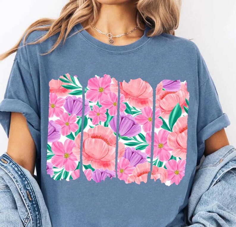 May include: A blue t-shirt with a floral print design. The print features pink, purple, and green flowers in a repeating pattern.