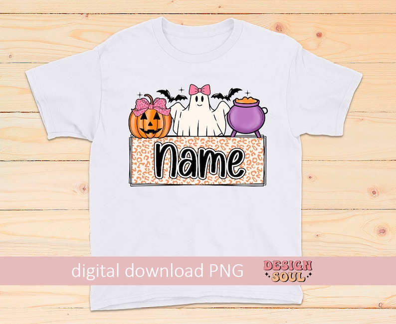 May include: A white t-shirt with a Halloween-themed design featuring a ghost, a pumpkin, and a cauldron. The design is on a leopard print background with the word "name" in black text.