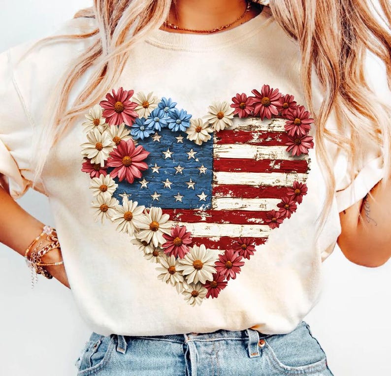 May include: Cream-colored sweatshirt featuring a heart-shaped design of the American flag, adorned with red, white, and blue flowers. The flag design has a distressed, vintage look, with visible stars and stripes.