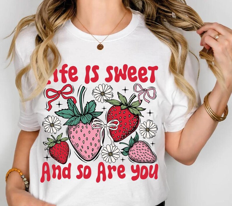 May include: White t-shirt with a red graphic that says "Life is sweet and so are you". The graphic features three strawberries with pink and red accents, green leaves, and white flowers.