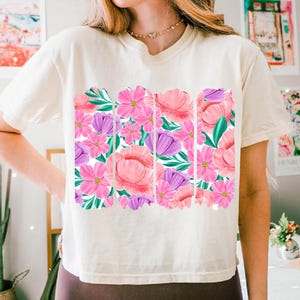 May include: A white t-shirt with a floral print featuring pink and purple flowers with green leaves.