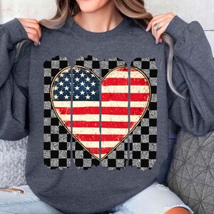 May include: A dark gray sweatshirt with a distressed American flag heart design. The heart is surrounded by a checkered pattern.