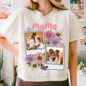 May include: Cream-colored t-shirt with the word "Mama" in pink script. The shirt features two framed photos of a mother and child, surrounded by pink, purple, and white flowers, and a butterfly.