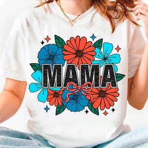 Pu&ograve; includere: Maglietta bianca con un design floreale e la parola "MAMA" in lettere di glitter nero.