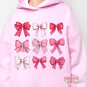 May include: Pink hoodie with a graphic print of nine pink bows in different styles. The text "DESIGN SOUL" is printed on the bottom right corner of the hoodie.