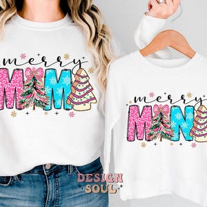 Peut inclure: Chemise &agrave; manches longues blanches avec un motif sur le th&egrave;me de No&euml;l. Les chemises pr&eacute;sentent le texte "merry" et "mama" avec des sapins de No&euml;l roses, bleus et verts.