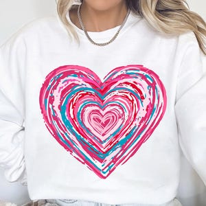 Pu&ograve; includere: Felpa bianca con un design a forma di cuore astratto in rosa, rosso e blu.