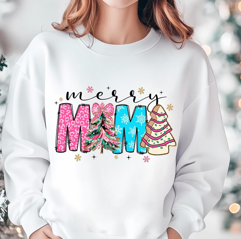 Peut inclure: Sweat-shirt blanc avec un motif de No&euml;l. Le texte "merry" est au-dessus du mot "MAMA" qui est d&eacute;cor&eacute; de sapins de No&euml;l roses, bleus et verts.