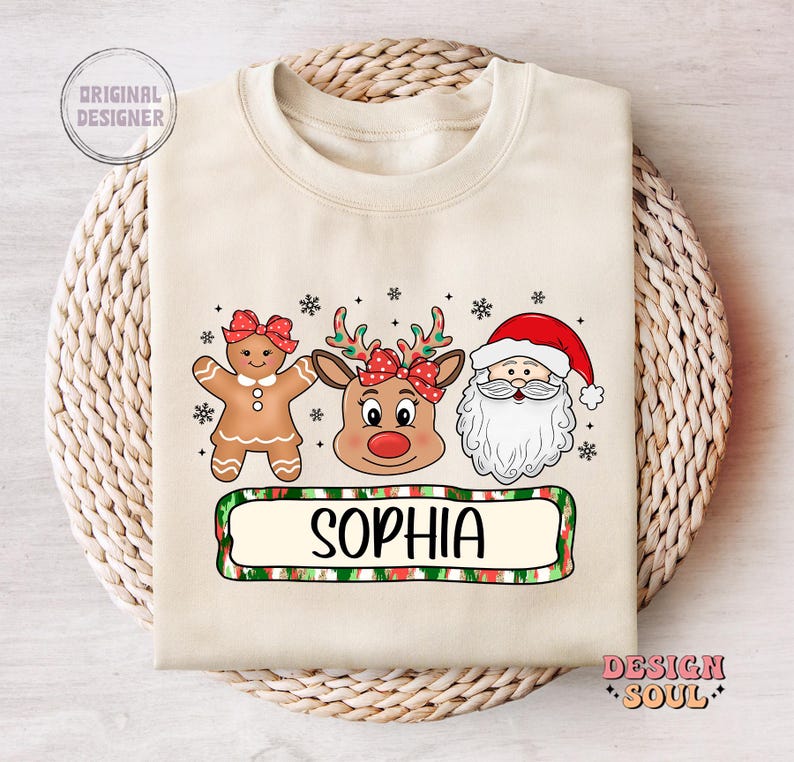 May include: A beige Christmas sweatshirt with a gingerbread person, reindeer, and Santa Claus illustration. The text "Sophia" is printed on a green and red striped banner.