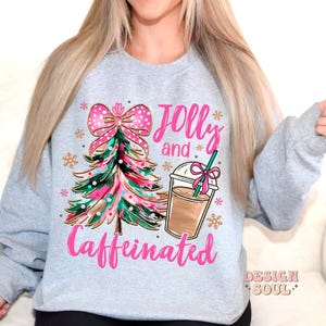 May include: A gray sweatshirt with a pink and green Christmas tree, a pink bow, and a cup of coffee. The text "Jolly and Caffeinated" is printed on the sweatshirt.