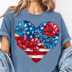 May include: A blue t-shirt with a red, white, and blue heart-shaped design. The heart is made up of painted flowers and an American flag.