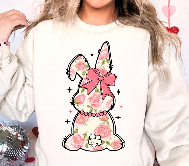 May include: White sweatshirt with a pink floral bunny graphic. The bunny has a pink bow and is surrounded by stars.