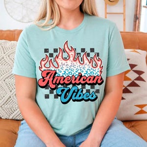 May include: A light blue t-shirt with a graphic of a red, white, and blue flame with a cheetah print design. The text "American Vibes" is printed in a retro font.