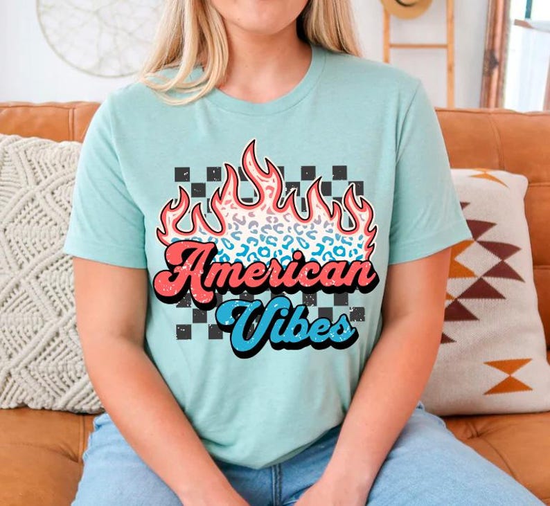 May include: A light blue t-shirt with a graphic of a red, white, and blue flame with a cheetah print design. The text "American Vibes" is printed in a retro font.